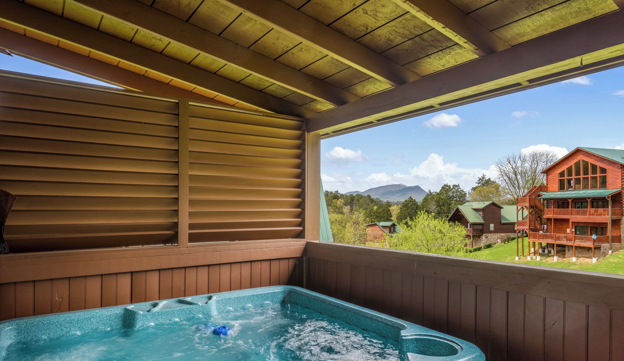 A hot tub in a wooden cabin with a view of a mountain and a red building in the background.