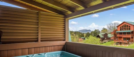 Un jacuzzi en una cabaña de madera con vistas a una montaña y un edificio rojo al fondo.