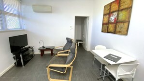 Una sala de estar moderna con televisión, dos sillones, una mesita y un cuadro en la pared.