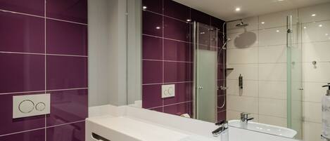 Un baño moderno con un espejo grande, un lavamanos blanco y una ducha con mampara de vidrio.