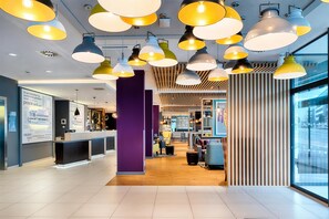 A modern hotel lobby with multiple seating areas, a reception desk, and a large window offering a view of the street. - Premier Inn Leipzig City Centre (Leipzig)