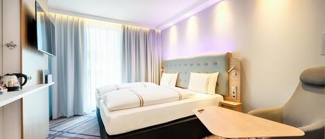 A hotel room with a bed, a desk, a chair, a TV, and a bedside table.