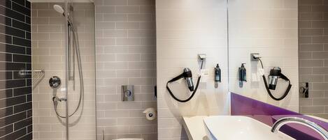 Un baño moderno con ducha de vidrio, lavamanos blanco con un detalle morado y un inodoro.