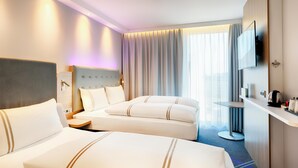 Hotellihuone, jossa on kaksi sänkyä, televisio, työpöytä ja suuri ikkuna, jossa on verhot.