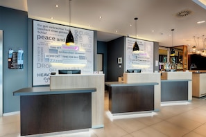 A hotel reception area with modern design, including a reception desk, a wall with motivational words, and a bar area in the background. - Premier Inn Leipzig City Centre (Leipzig)