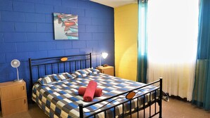 Ein Schlafzimmer mit kariertem Bettbezug, einem roten Handtuch, zwei Nachttischlampen, einem Nachttisch und einem Bild an der Wand.