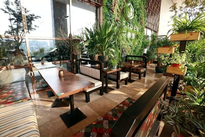 Un restaurante con mesas y sillas de madera, asientos interiores y plantas en macetas.
