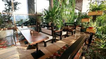 Un restaurante con mesas y sillas de madera, asientos interiores y plantas en macetas.