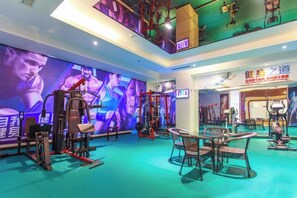 A gym with exercise equipment, a mirrored wall, and a ceiling with a light fixture. - Huaxin Hotel (XIANNING)