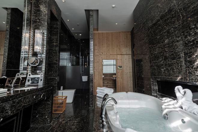 A modern bathroom with a marble countertop, a large bathtub, and a wooden panel wall.