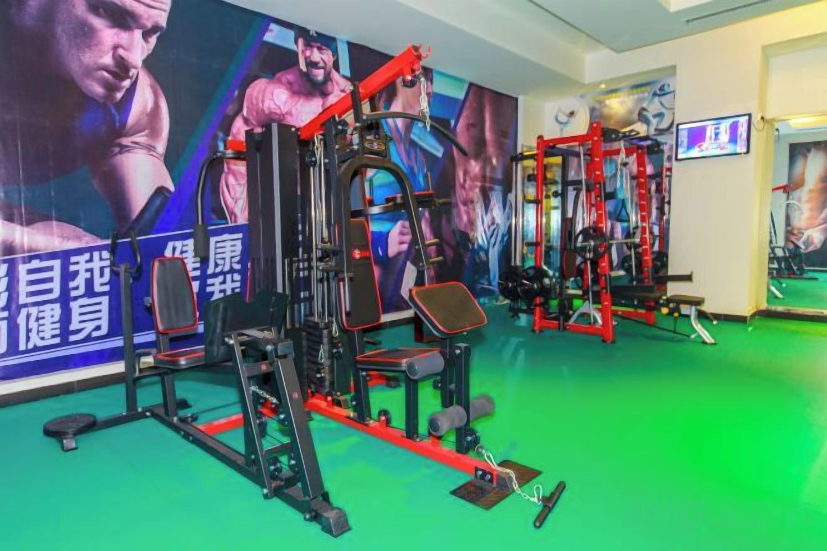 Un gimnasio con equipo de ejercicio, un espejo grande y carteles motivacionales en la pared.