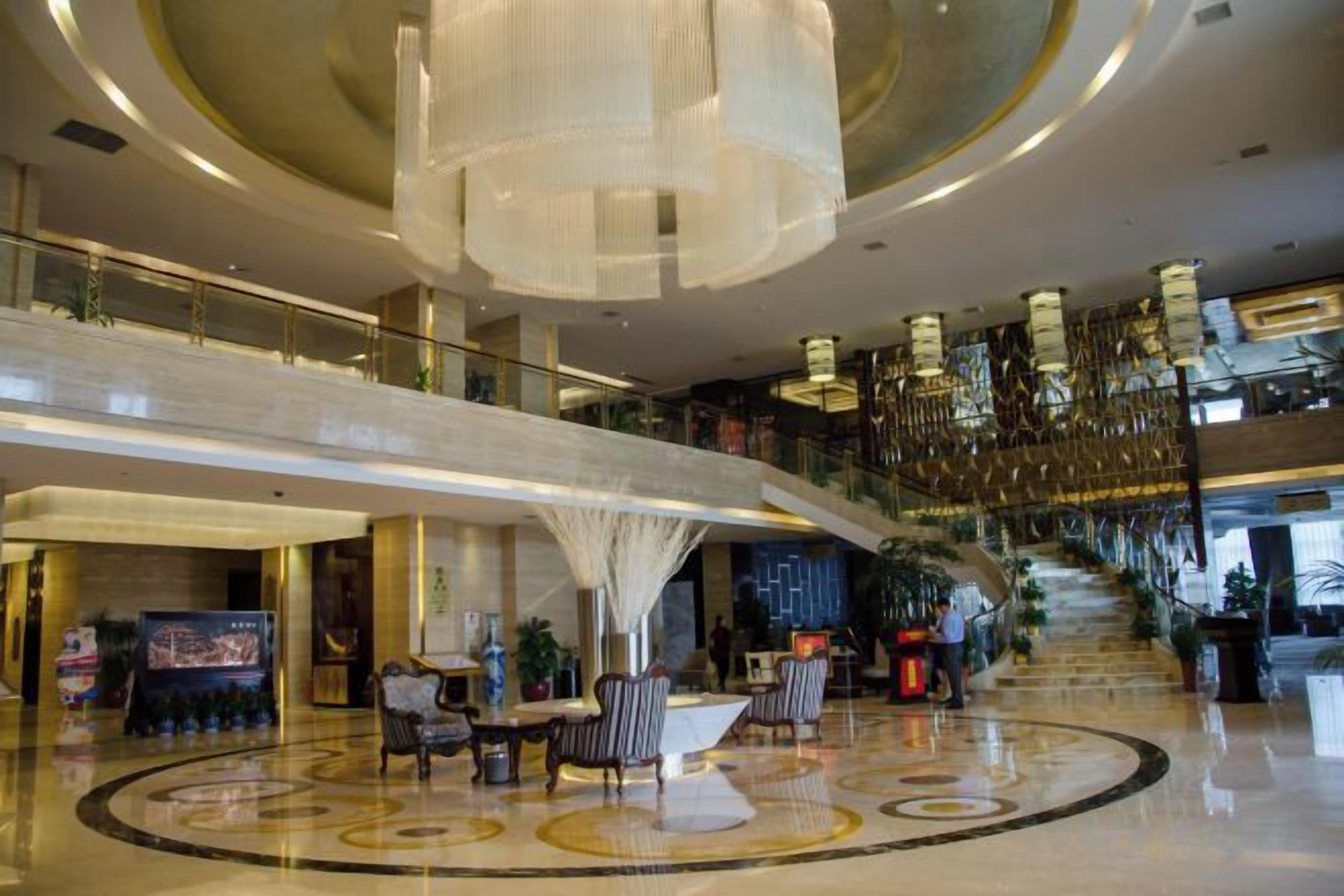 A spacious lobby with a central seating area, a staircase, and a high ceiling with hanging lights.