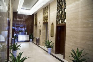 A hotel lobby with a marble floor, potted plants, and a reception desk. - Huaxin Hotel (XIANNING)