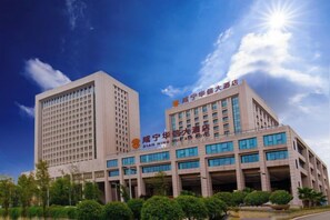 A multi-story building with a prominent entrance and signage, surrounded by greenery. - Huaxin Hotel (XIANNING)
