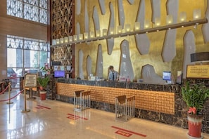 A reception area with a marble counter, a receptionist, and a large window. - Huaxin Hotel (XIANNING)