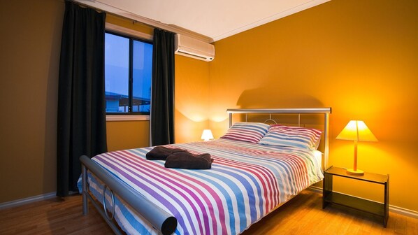 Una habitación de hotel con cama, mesita de noche, lámpara y ventana con cortinas.
