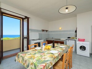 A compact kitchen with a dining area, a washing machine, and a view of the sea.