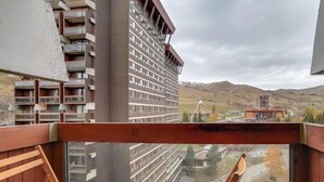 Un balcó amb mobles de fusta, dues tasses vermelles i vista d'un edifici d'àmples proporcions i un paisatge amb turons.