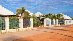 A row of white-roofed buildings with blue gates, surrounded by palm trees and a clear sky. - Osprey Holiday Village Unit 203/1 Bedroom - Villa with a Pool in the Complex (EXMOUTH)