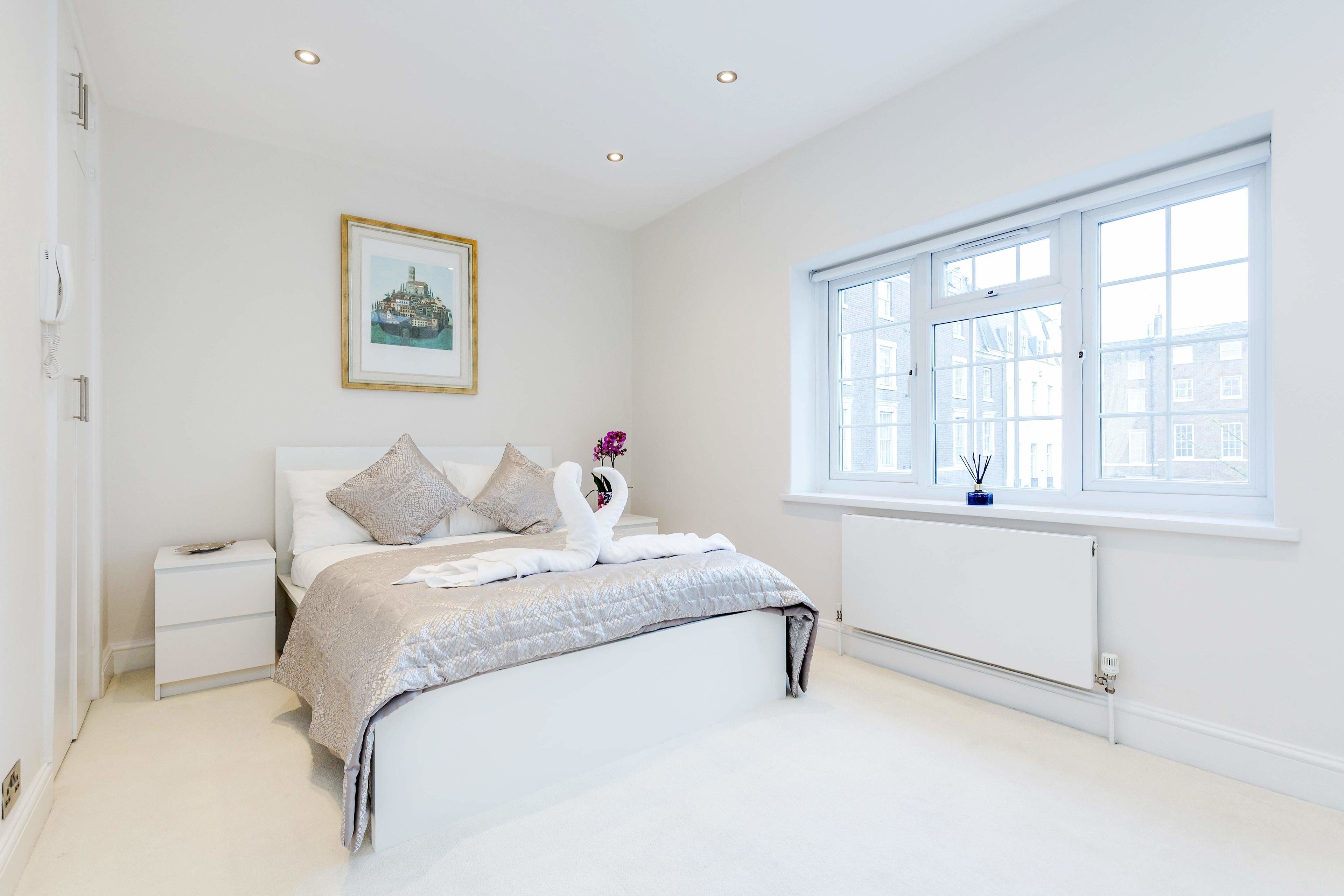 A bedroom with a bed, bedside tables, a window, and a framed picture on the wall.