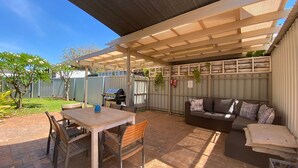 Eine Terrasse im Freien mit Holztisch und -stühlen, einem Grill und einer Couch mit Kissen.