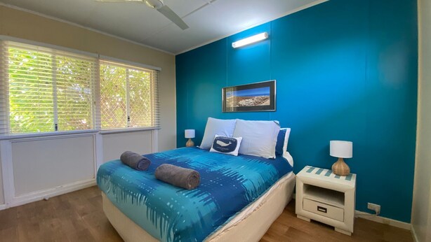 Ein Schlafzimmer mit einem Bett, zwei Nachttischen, einem Fenster mit Jalousien und einem gerahmten Bild an der Wand.
