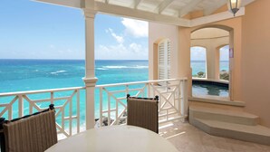 A covered outdoor area with a view of the ocean, a pool, and a table with chairs.