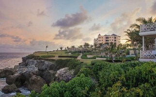 Un hotel costero con un edificio grande, palmeras y una costa rocosa.