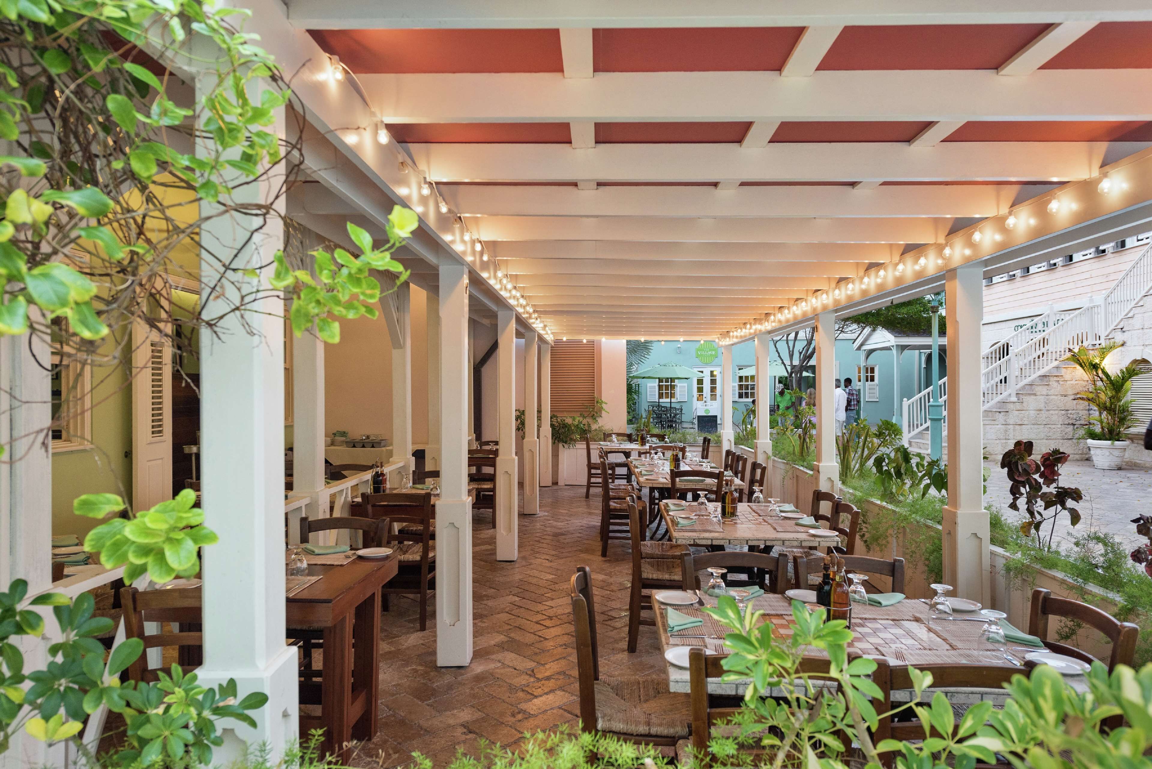 An outdoor dining area with wooden tables and chairs, a brick floor, and string lights.
