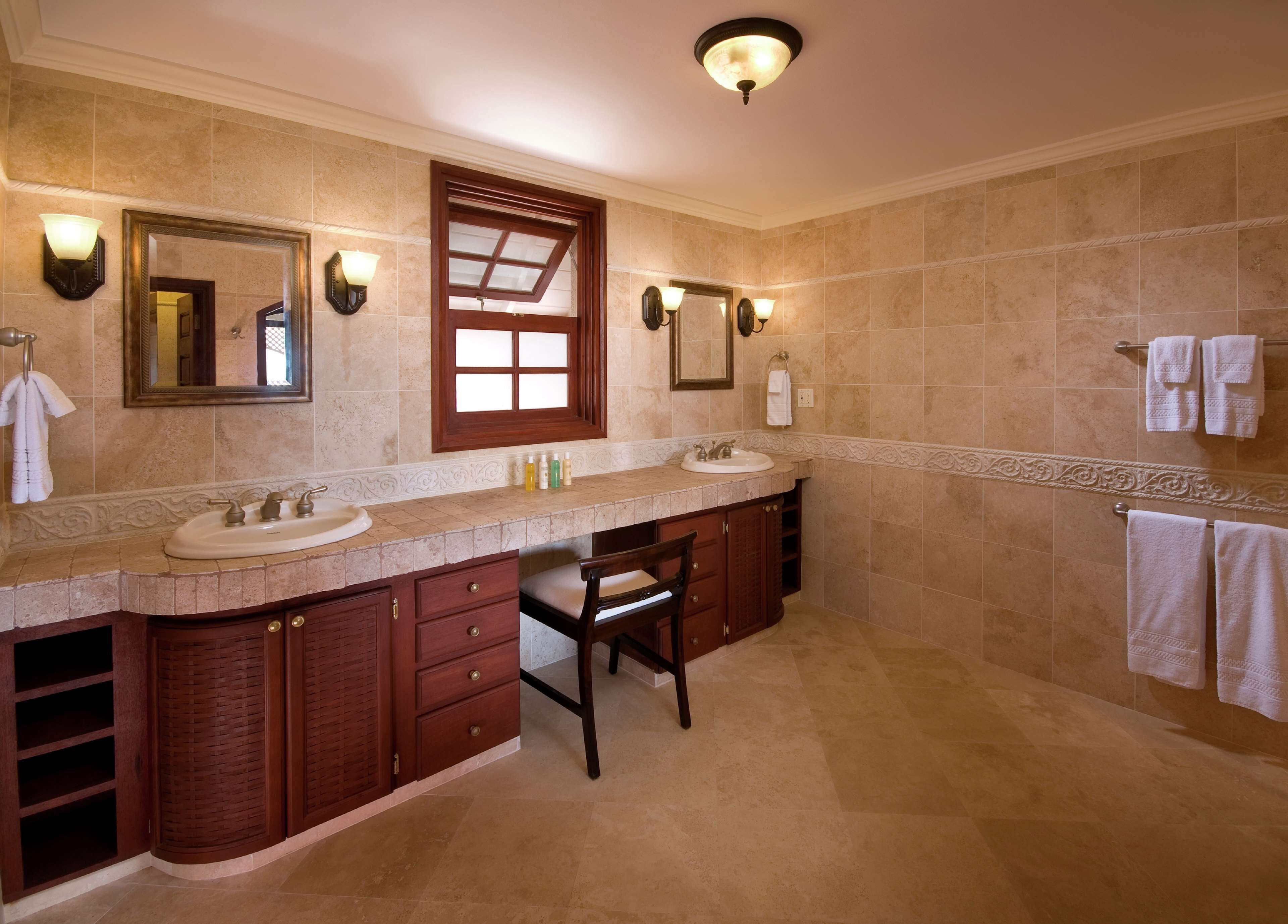 A spacious bathroom with two sinks, a vanity with drawers, a chair, and a large mirror.