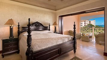 Un dormitorio con una cama grande, dos mesitas de noche con lámparas, un ventilador de techo y vista al océano a través de una puerta abierta.