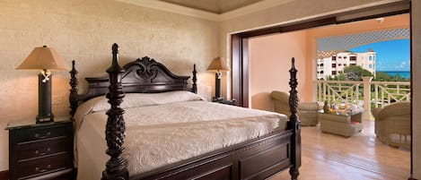 Un dormitorio con una cama grande, dos mesitas de noche con lámparas, un ventilador de techo y vista al océano a través de una puerta abierta.