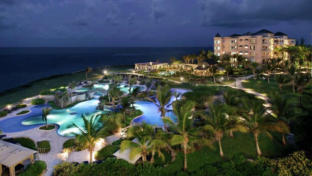 A resort with multiple swimming pools, a large building with multiple balconies, and a view of the ocean.
