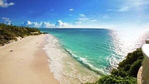 A beach with clear turquoise waters, a sandy shore, and lush greenery.