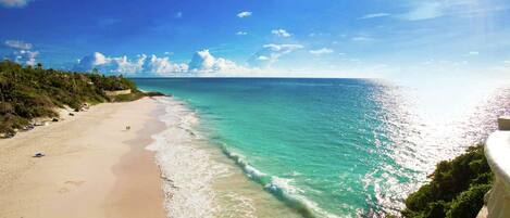 Een strand met helder turquoise water, een zandstrand en weelderige begroeiing.