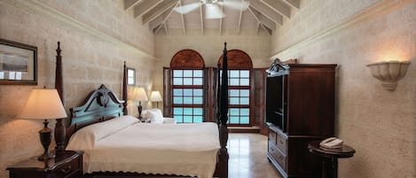 Un dormitorio amplio con una cama grande, un ventilador de techo y vistas al mar a través de ventanales arqueados.