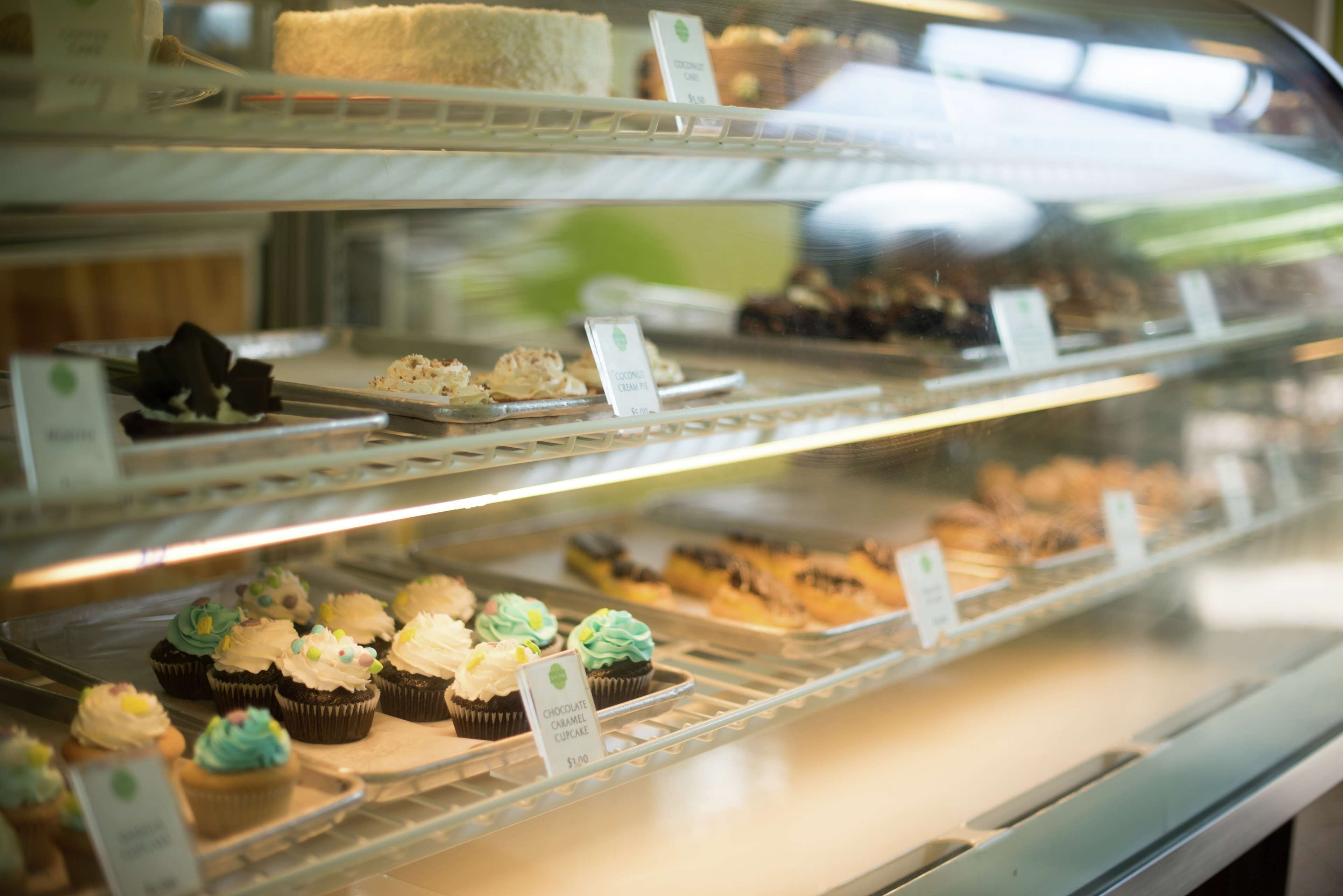 A bakery display case with various pastries and desserts, including cupcakes and cakes, with price tags visible.