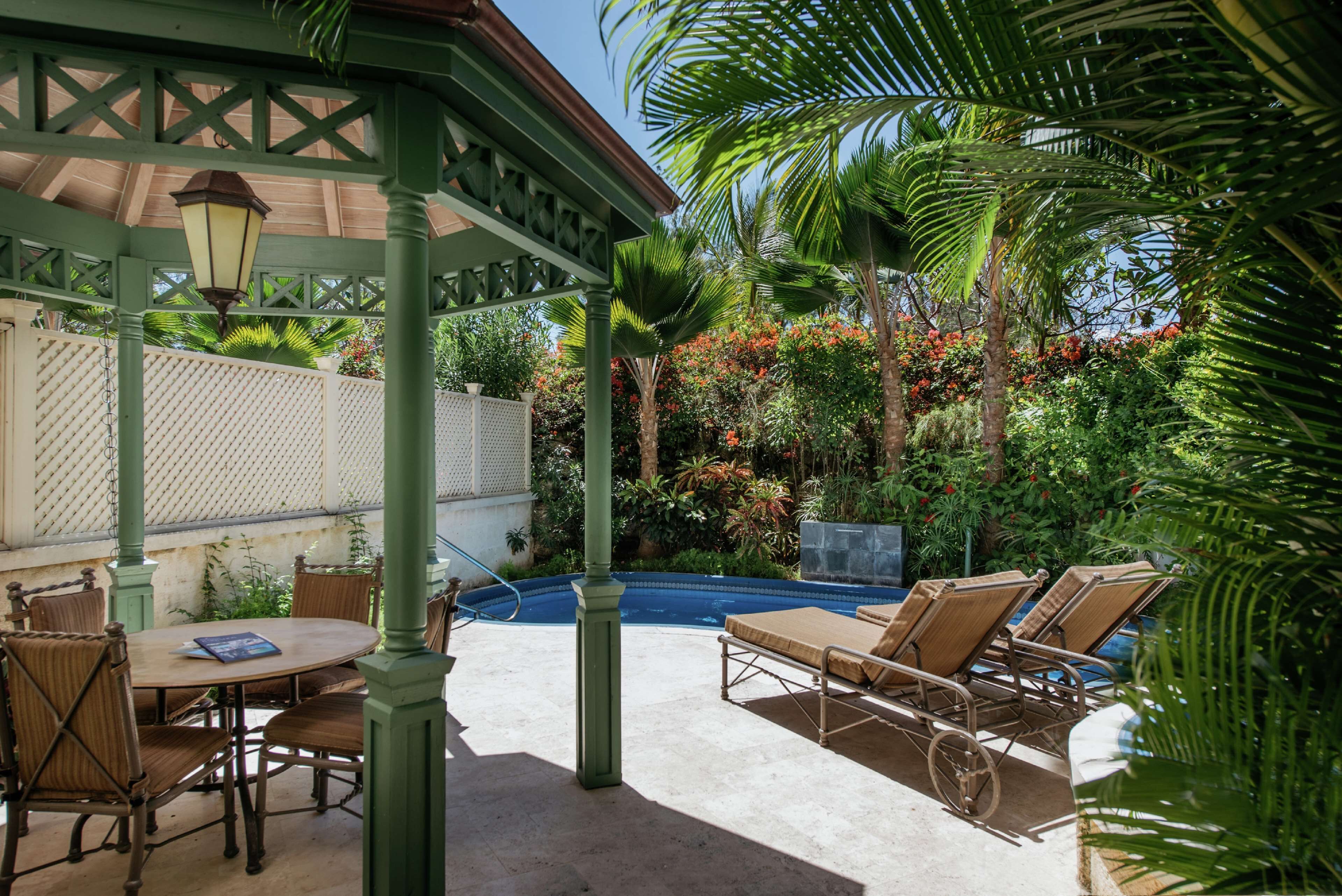 A covered patio area with a pool, lounge chairs, and a table with chairs.