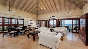 A spacious living room with high ceilings, a chandelier, and a view of the ocean through large windows.