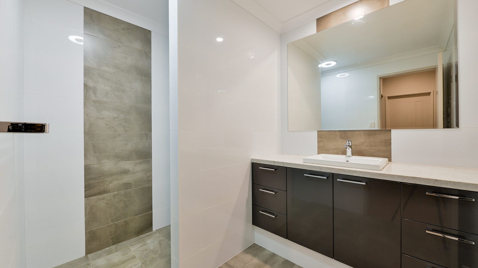 A modern bathroom with a large mirror, a sink, and dark cabinets.