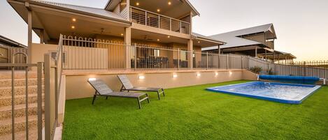 Una casa de dos pisos con piscina, un patio cubierto y un césped bien cuidado.