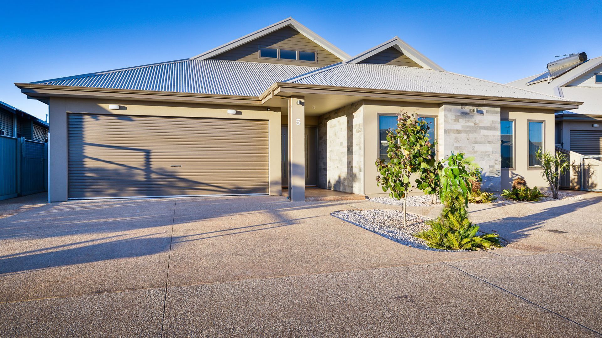 A modern two-story house with a garage, a covered driveway, and a small garden with a palm tree.