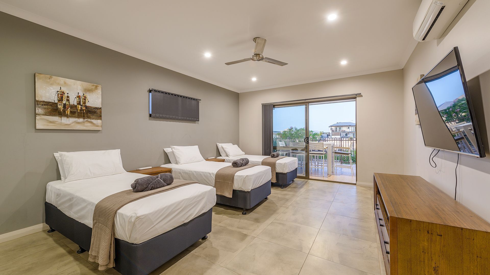 A modern hotel room with two beds, a ceiling fan, an air conditioning unit, a TV, and a balcony with a view of the city.