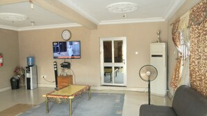 Una sala de estar con sofá, mesa de centro, televisor, dispensador de agua y ventilador.