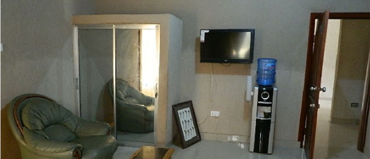 Una sala de estar con un sofá, un televisor montado en la pared, un dispensador de agua y una puerta que da a otra habitación.