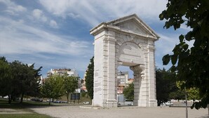 Ein Steinkunstwerk in Form eines Bogens in einem Park mit einem gepflasterten Weg und Bäumen.