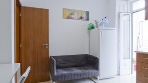 Ein Zimmer mit Holztür, grauem Sofa, weißem Kühlschrank und einem Fenster mit Tageslicht.