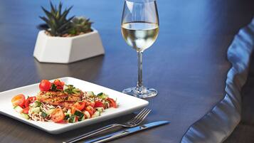 A dining table with a plate of food, a glass of white wine, and a small potted plant.