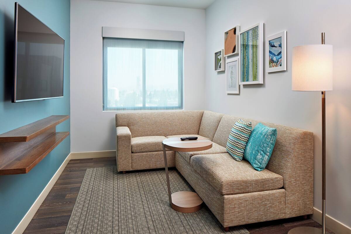 A modern living room with a sectional sofa, a small round table, a mounted TV, and a floor lamp.