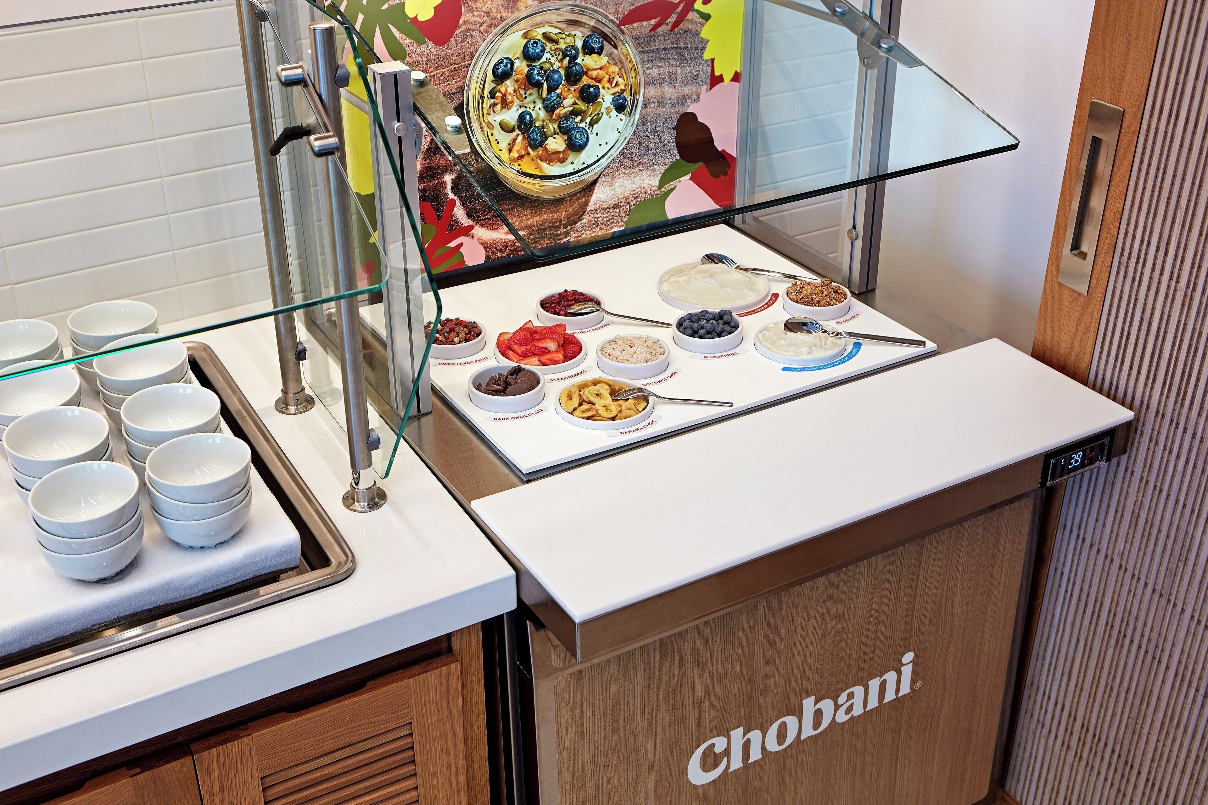 A buffet counter with various food options, including yogurt, fruits, and chocolate.
